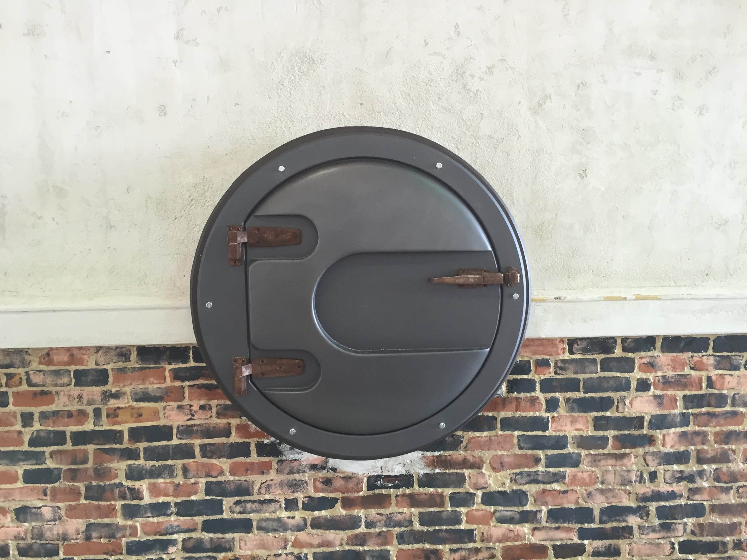 The finished hatch hung against the dressed wall — painted brick wainscot below, aged plaster above.