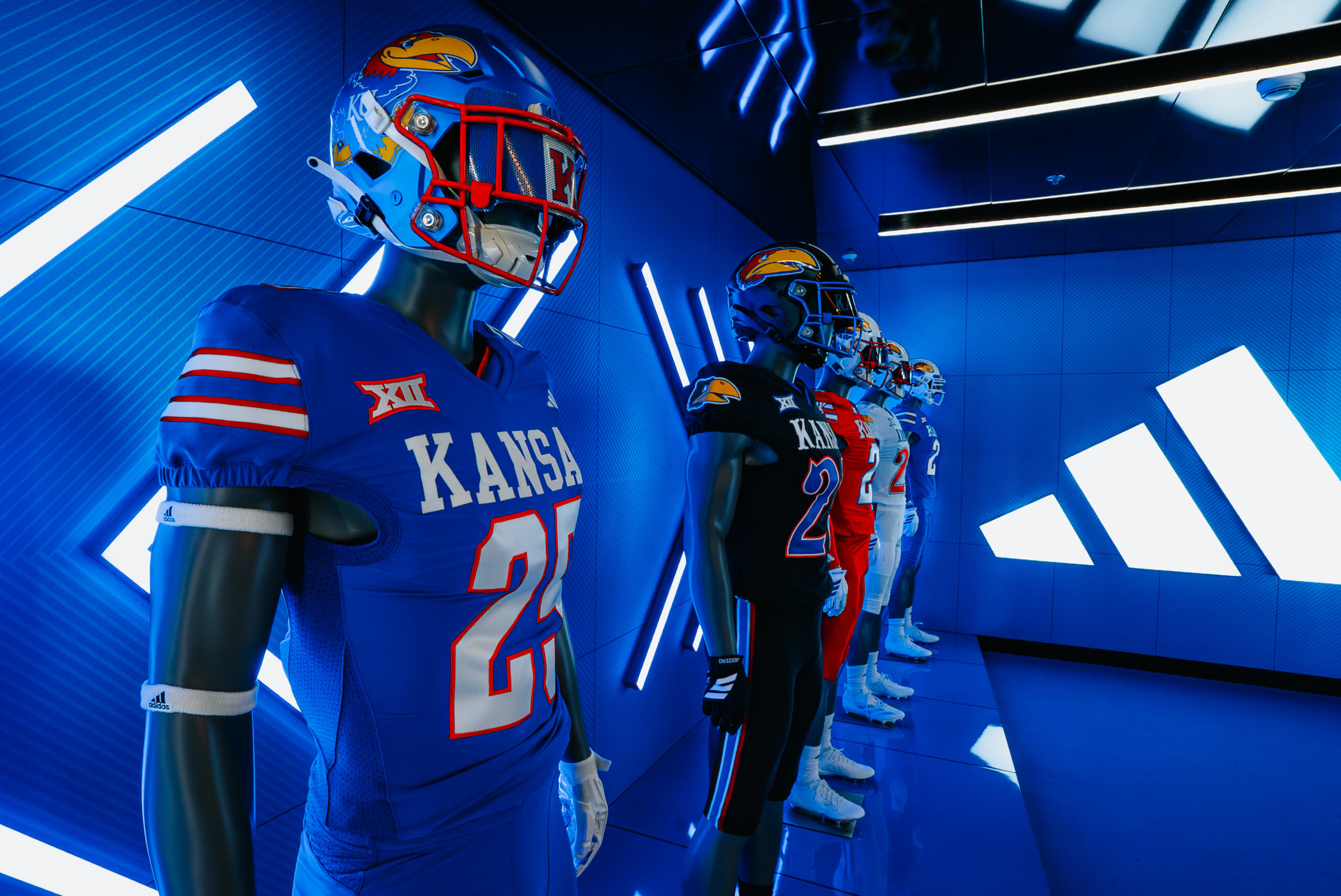 Close-up down the mannequin line; a Jayhawk-wrapped helmet with a red facemask sits in the foreground.