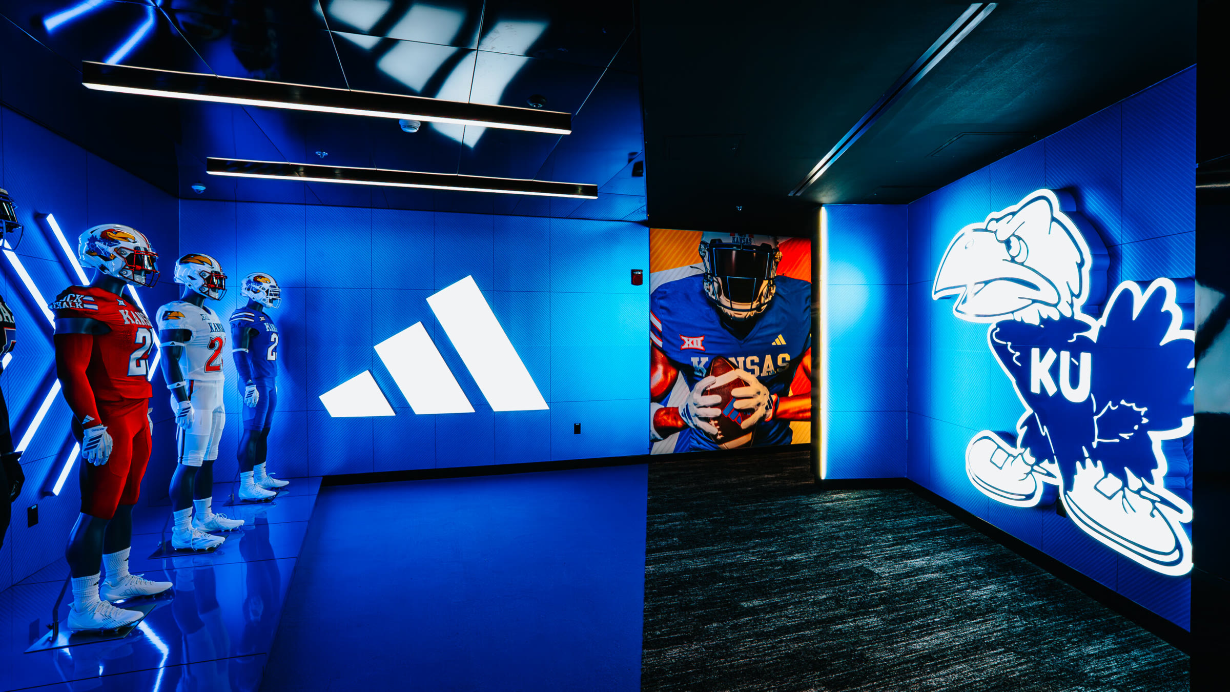 Gear display, reverse angle: the mannequin line, the backlit adidas wall, and the mural-and-Jayhawk corner in a single frame.