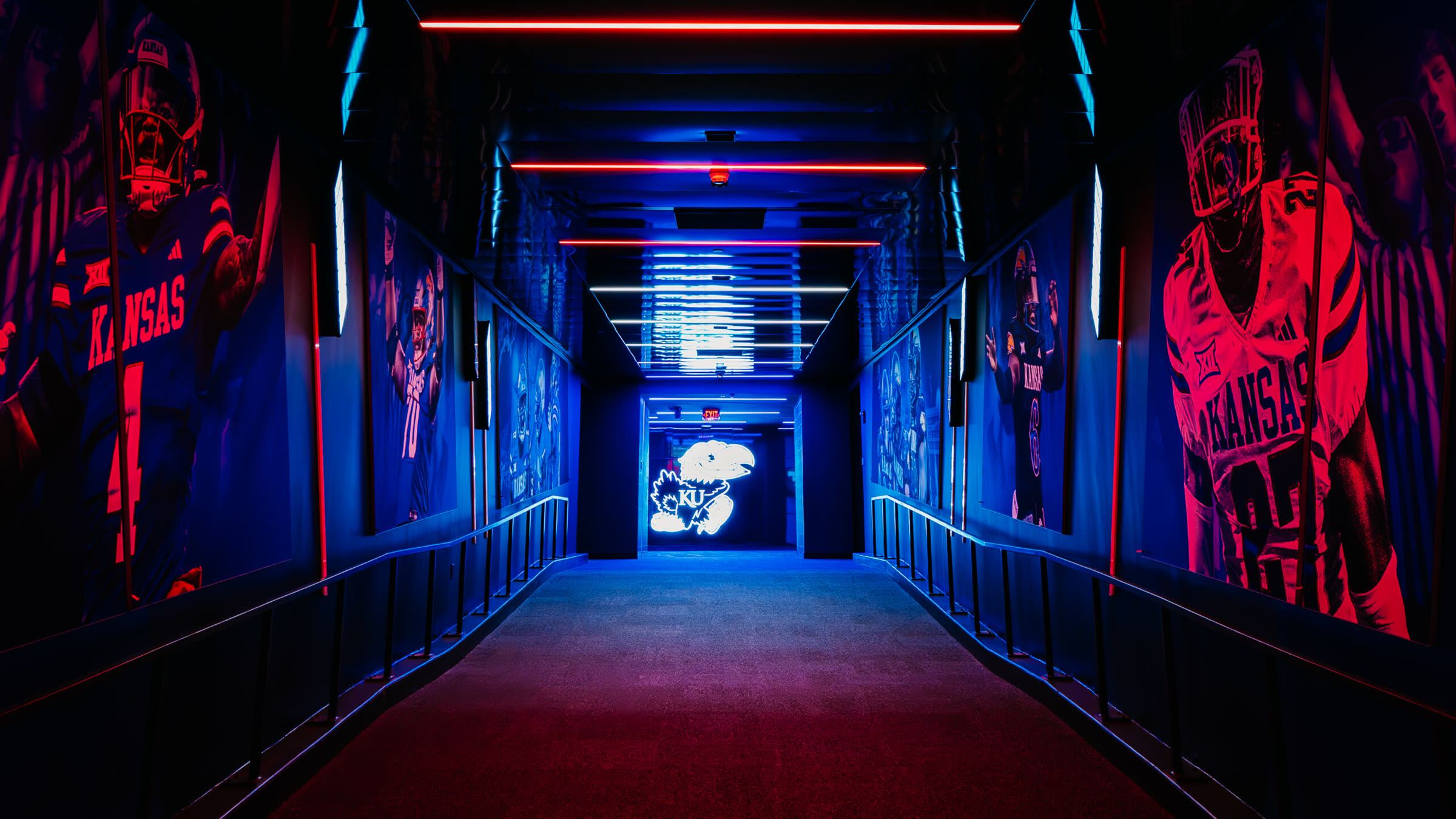 Looking back up the hype tunnel mid-change, red shifting to blue, the mirrored backlit Jayhawk centered in the tunnel entrance.