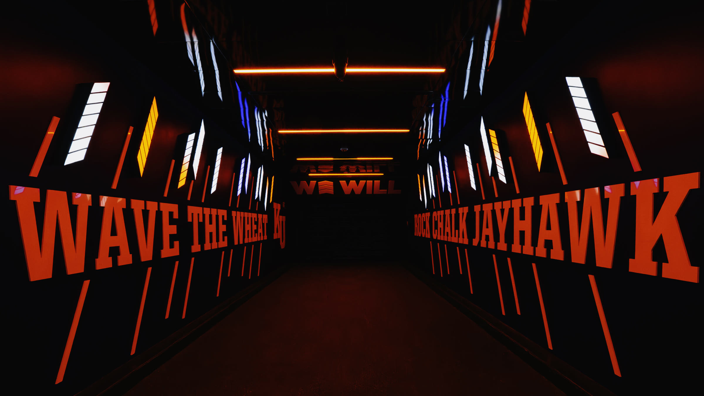 Hype tunnel in its red state: WAVE THE WHEAT and ROCK CHALK JAYHAWK letterforms lit red down both walls, the WE WILL sign at the end of the tunnel.
