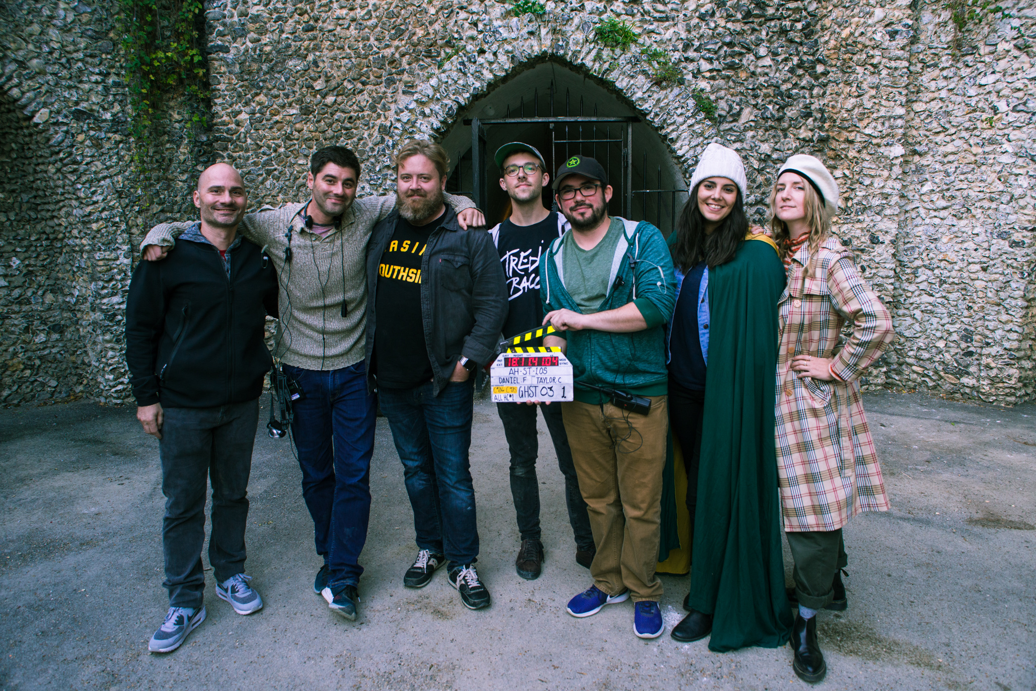 The seven Haunter department heads shoulder to shoulder in front of a flint-stone archway on location, one holding the production clapperboard.