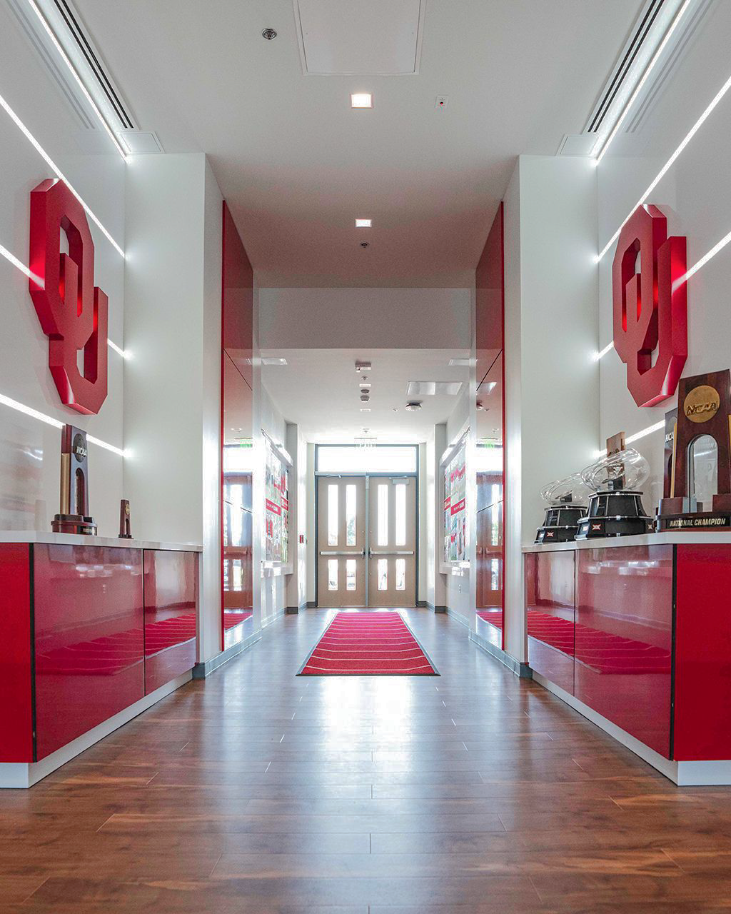 Ransom House entry hall: twin dimensional OU monograms flank a corridor of trophy cases lined with horizontal light bars, at the point where the men's and women's wings meet.