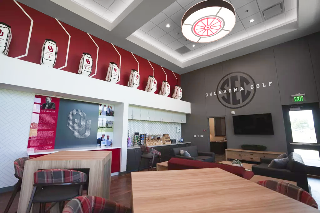 Jerry Ransom heritage wall, mirroring Coe's: a second golf-tee OU monogram on gray, a bio panel, a photo collage, and a coffee-bar kitchenette with a penny-round tile backsplash.