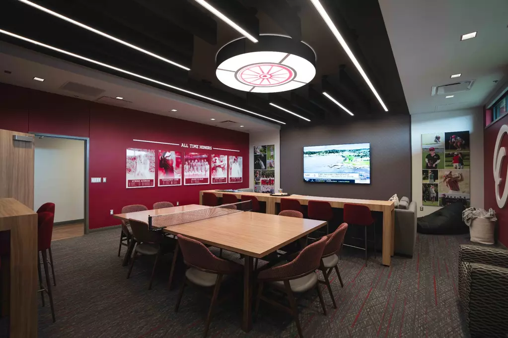 Women's lounge: a red feature wall headed 'ALL TIME HONORS' with five red-tinted player posters, photo-collage columns, a ping-pong table, and a wagon-wheel light fixture.