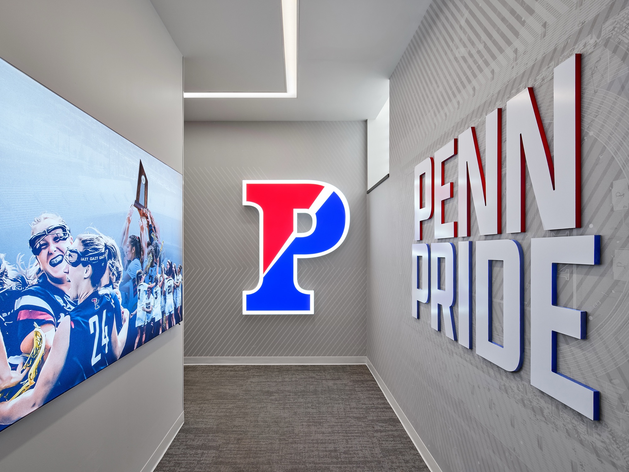 The entrance: a backlit red-and-blue split P on the end wall, dimensional PENN PRIDE letters along the right wall, and a backlit photograph of players raising a trophy on the left.