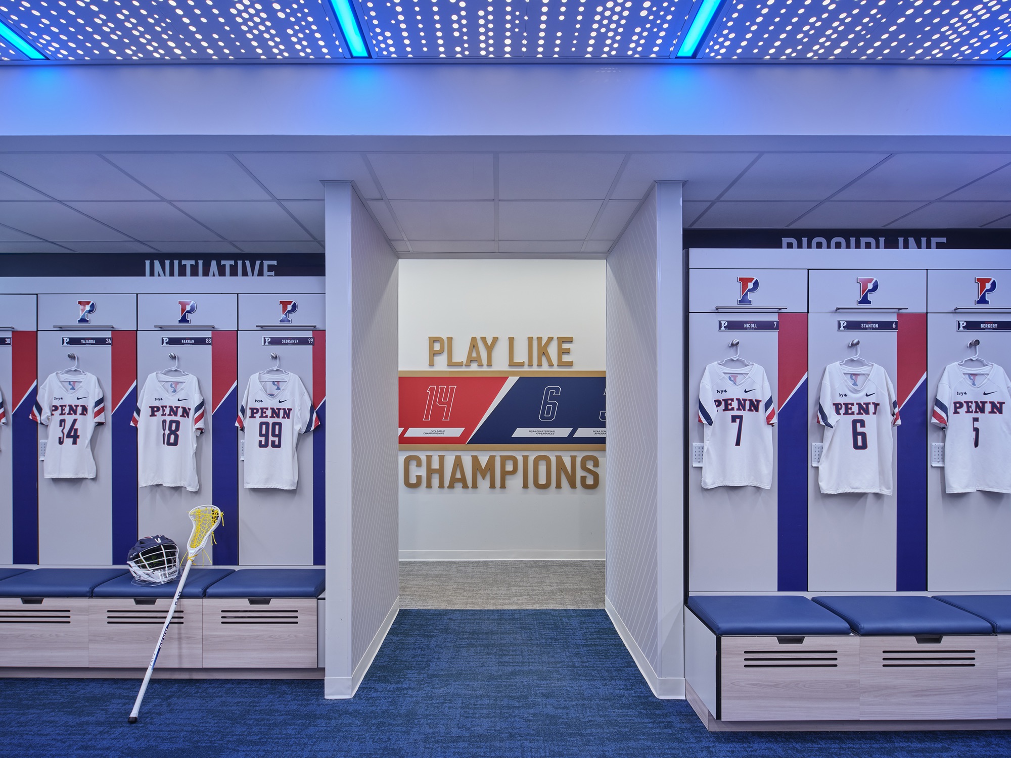 White game jerseys numbered 34, 18, 99, 7 and 6 hang in open lockers under a blue-lit perforated ceiling; through the center opening, a graphic reads PLAY LIKE CHAMPIONS.