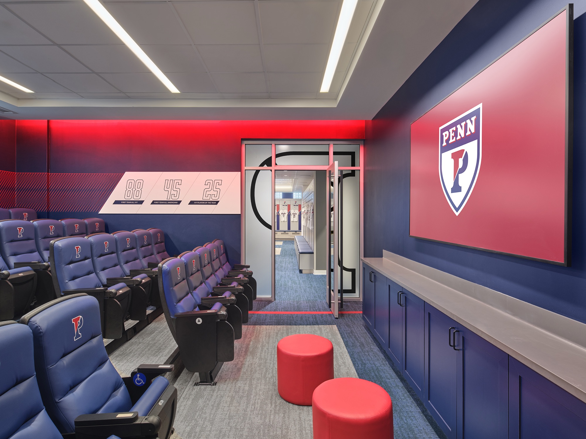 The team room from the side: tiered blue seats, a wall monitor carrying the Penn shield, red ottomans, and a numbers graphic reading 88, 45, 25 on the far wall.